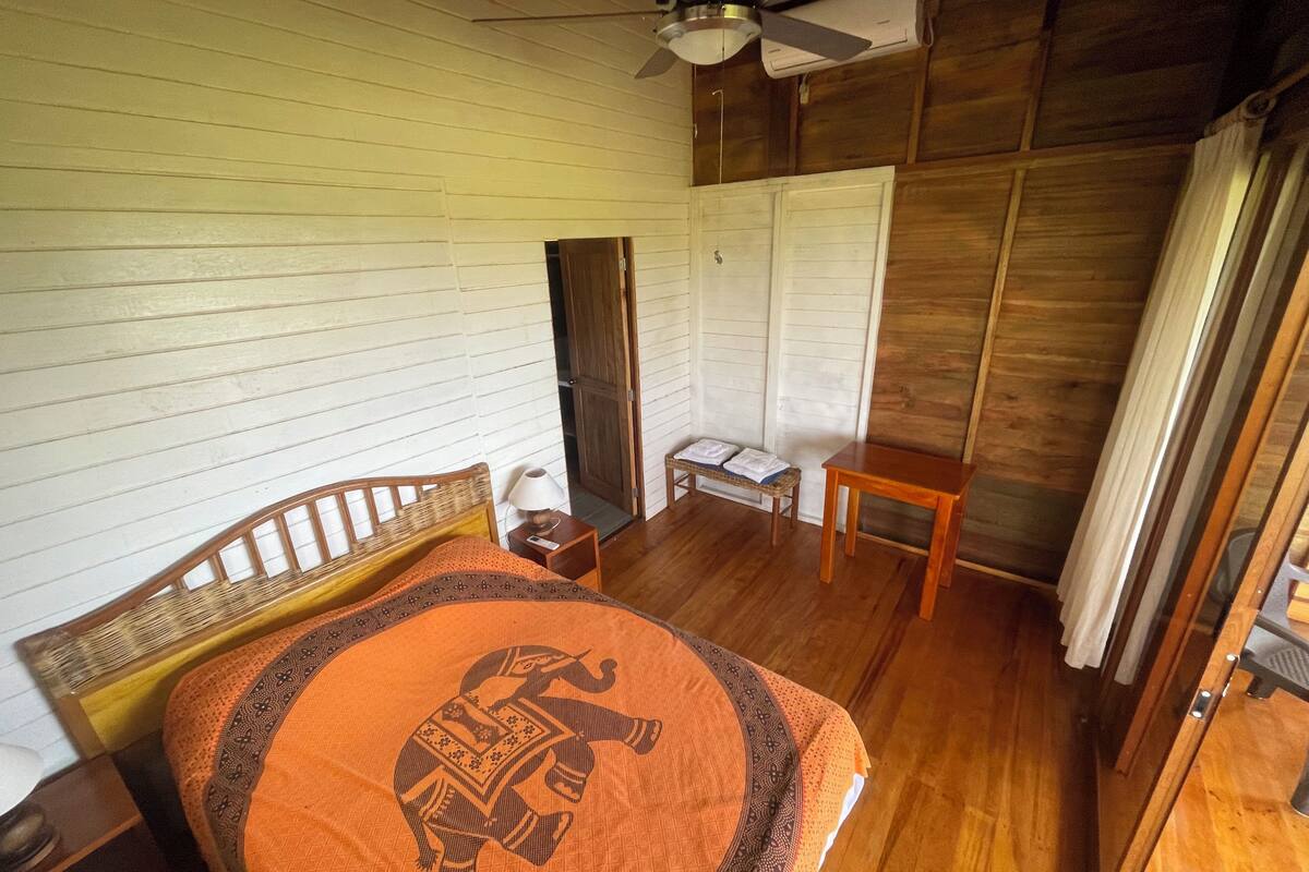 Een houten kamer met een bed, nachtkastje, een klein tafeltje en een kledingkast.