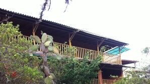 A wooden house with a balcony, surrounded by various plants and a red flower pot. - Galapagos Chalet (Puerto Ayora)