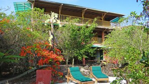 A wooden building with a balcony, surrounded by lush greenery and red flowering plants. - Galapagos Chalet (Puerto Ayora)