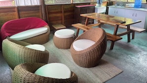 A cozy room with wicker furniture, a wooden table, and a view of greenery outside. - Galapagos Chalet (Puerto Ayora)
