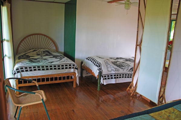 A room with two beds, a wooden chair, and a ceiling fan. - Galapagos Chalet (Puerto Ayora)