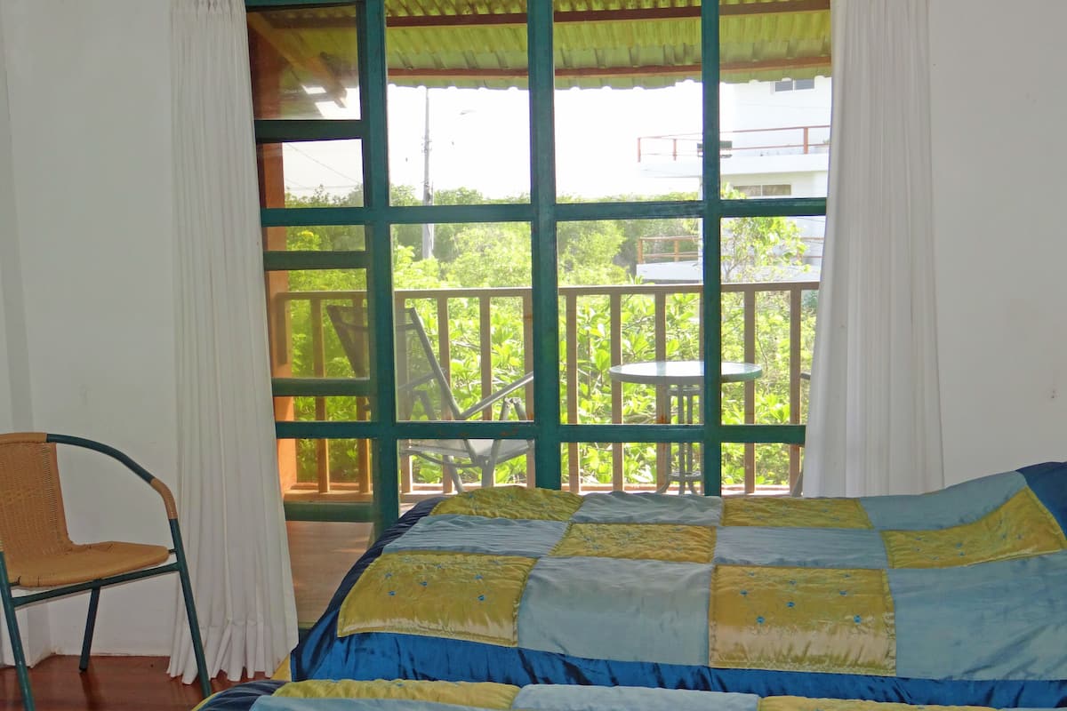 Een kamer met een bed, een stoel en grote ramen met uitzicht op groen en een balkon.
