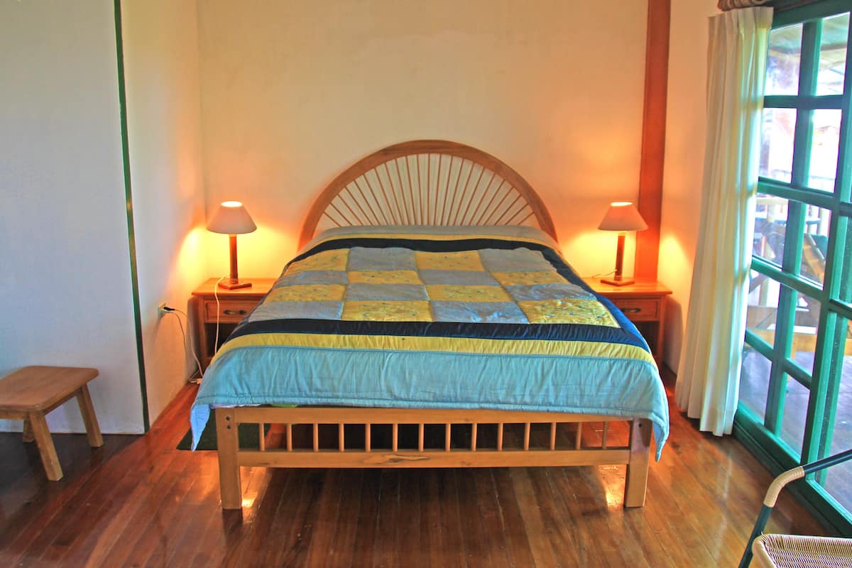 Een houten bed met een sprei, twee bedlampen en een raam met gordijnen.