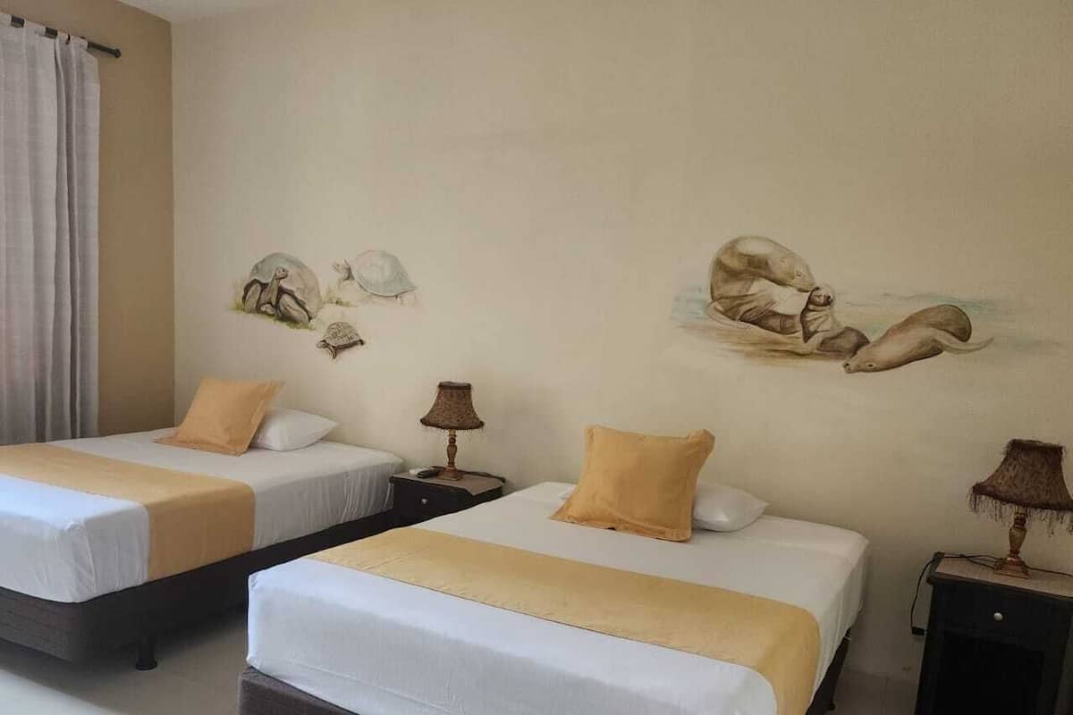 Quarto de hotel com duas camas, paredes bege e um mural de criaturas marinhas.