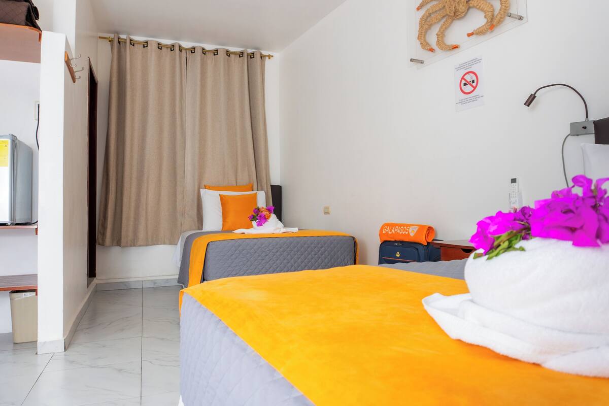 A hotel room with two beds, a TV, a desk, and a shower area.