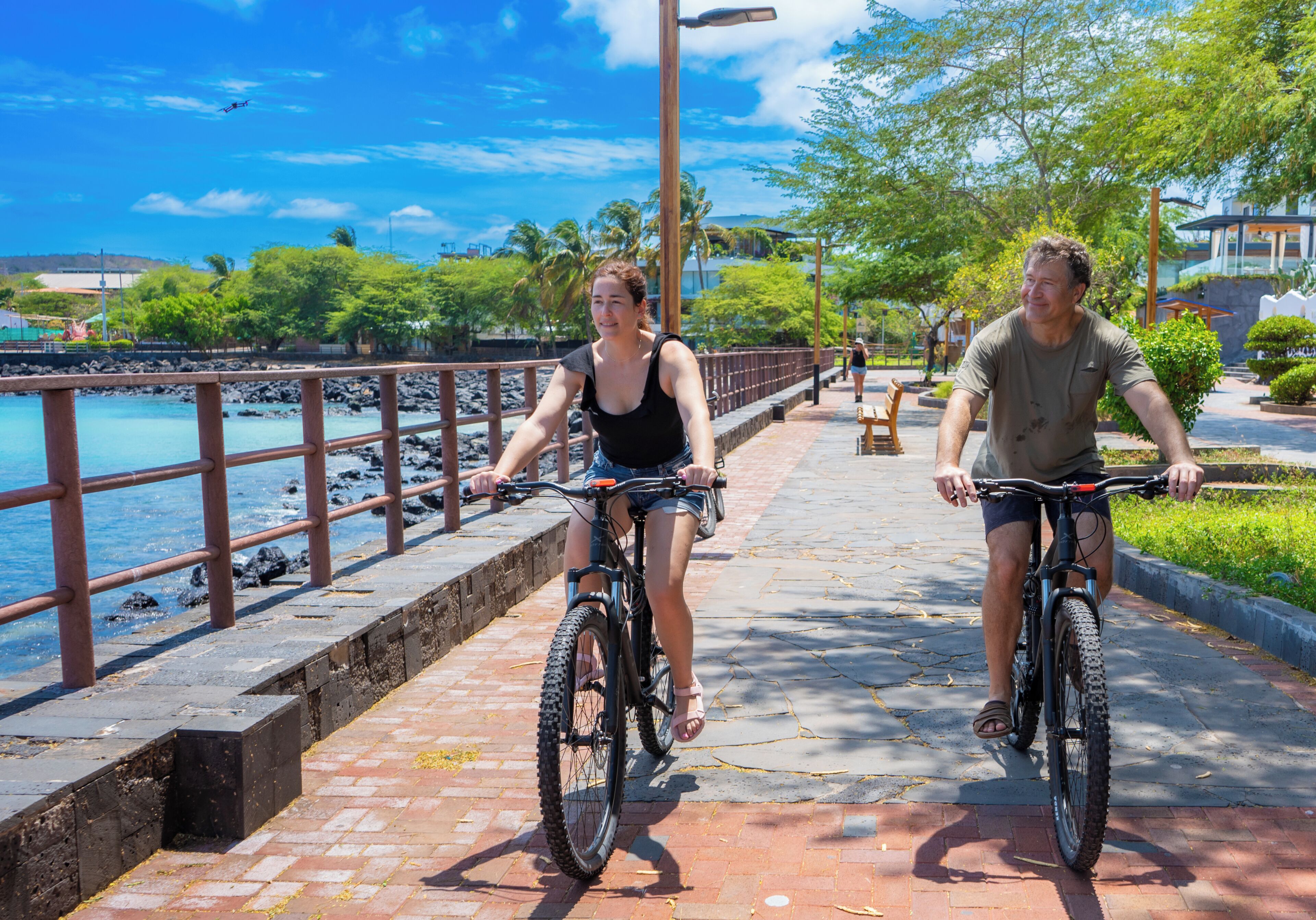 Two people riding bicycles on a paved pathway by a body of water.