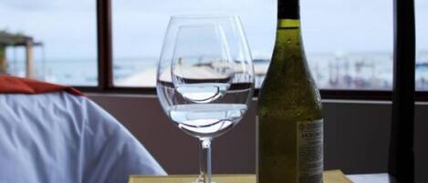 Una mesa con una copa de vino y una botella, una ventana con vista al mar y una silla de madera.