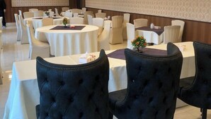 Un salón de banquetes con mesas redondas y sillas tapizadas en negro, unidades de aire acondicionado en las paredes e iluminación empotrada en el techo.