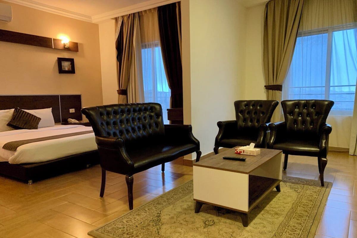 A hotel room with a bed, two leather armchairs, a coffee table, and a rug.