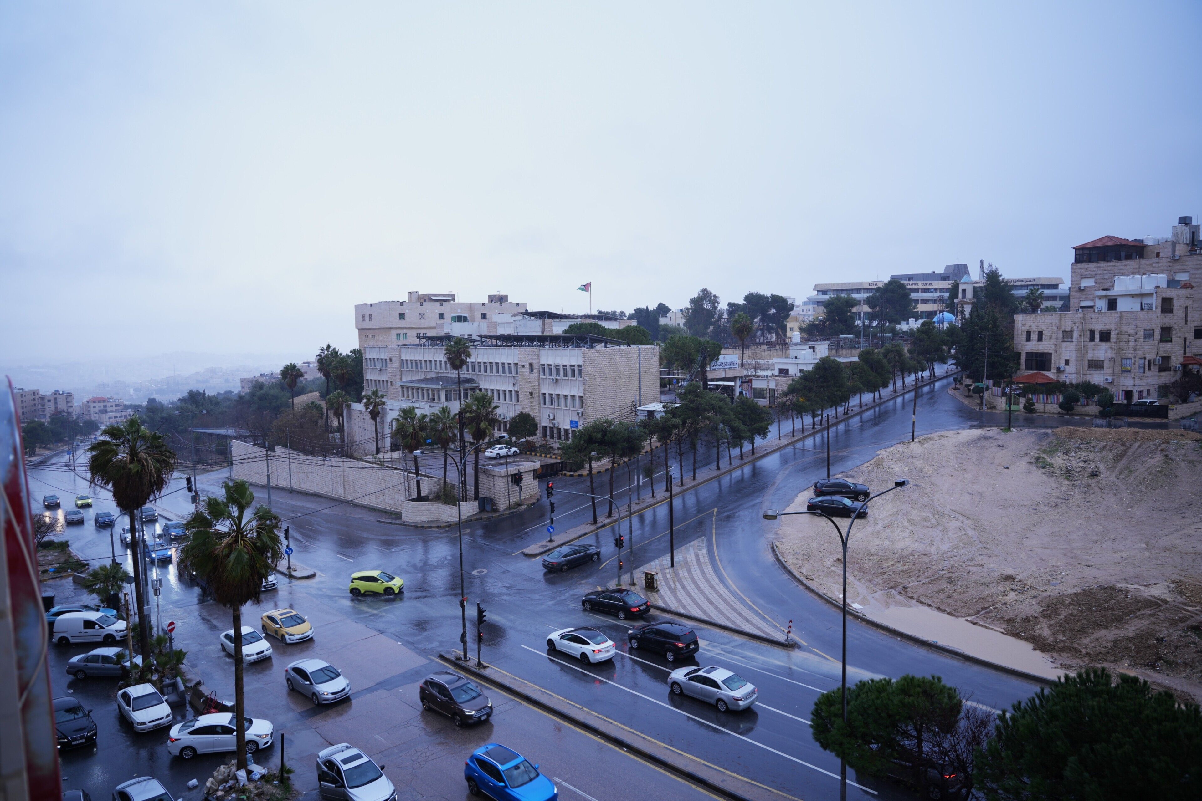 A city street with multiple lanes of traffic, palm trees, and buildings in the background.