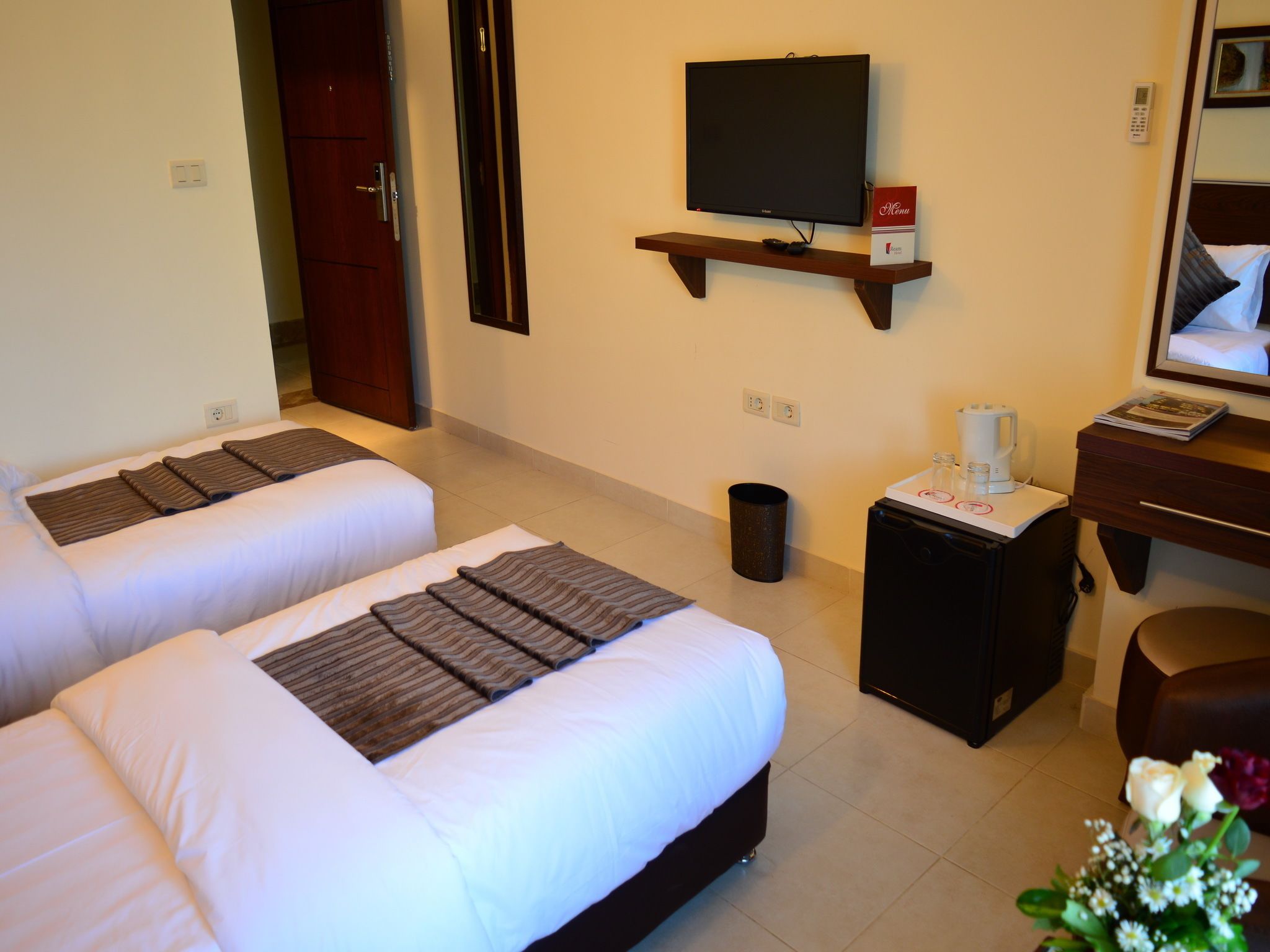 A hotel room with two single beds, a TV on a shelf, a coffee maker, and a trash can.