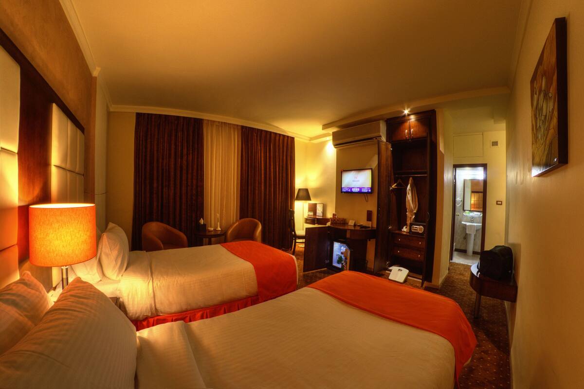A hotel room with two beds, a desk, a chair, a television, and a bathroom visible through an open door.