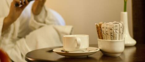 A cup of coffee, a small bowl of coffee pods, and a white vase with a flower on a table.