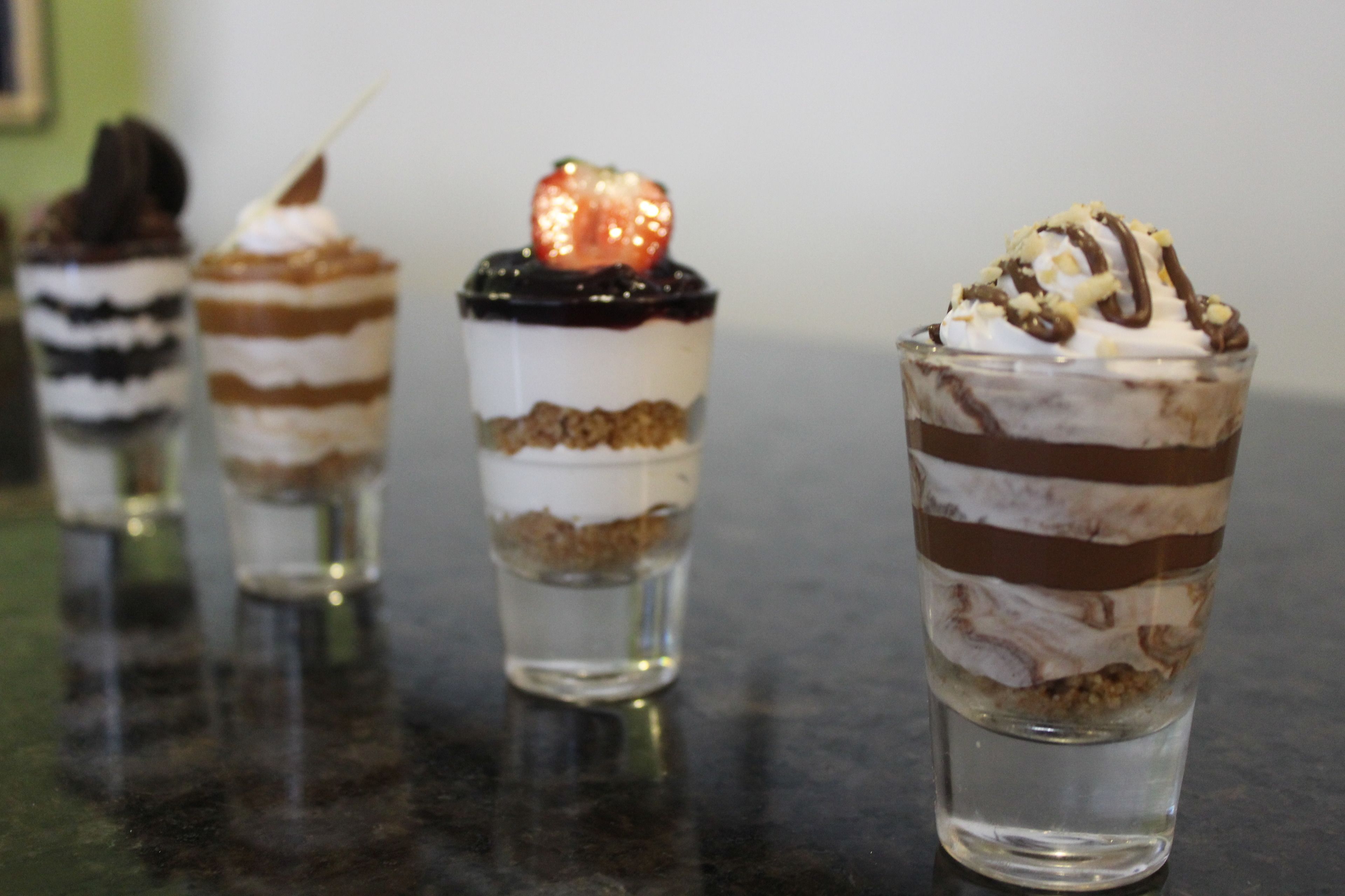 Four layered desserts in shot glasses.
