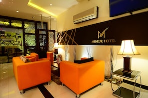 A modern hotel lobby with orange sofas, a glass table with a lamp, and a decorative wall with the hotel name. - Meneur Hotel (Amman)
