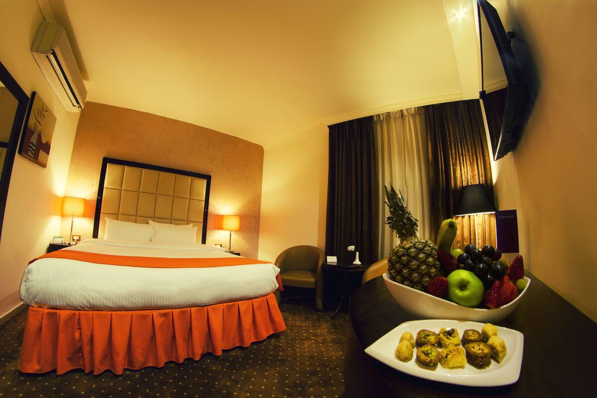 A hotel room with a bed, a desk with a fruit bowl, a chair, and a TV on the wall.