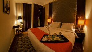 Et hotelværelse med en stor seng, et natbord med lampe, en stol og et bakke med morgenmad.