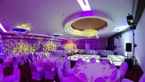 En festsal med runde borde, hvide stole og en scene med lys.