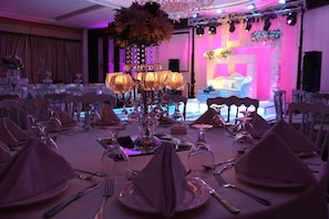 A banquet hall with round tables set for a formal event, featuring crystal chandeliers and floral centerpieces. - Meneur Hotel (Amman)