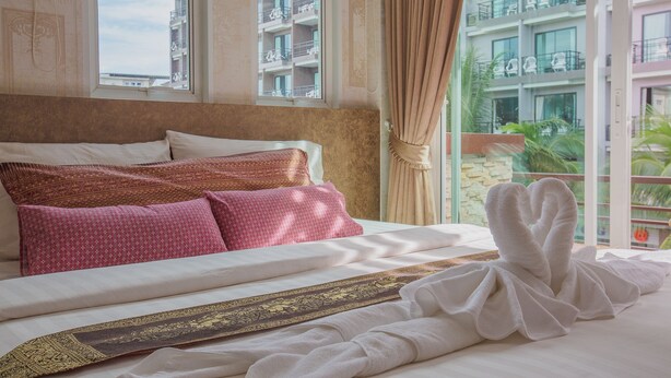 A hotel room with a large bed, a view of a building with balconies, and a window with curtains. - Jasmine House @ Pattaya (Pattaya)