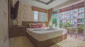 A hotel room with a bed, a TV mounted on the wall, a balcony with a view of other buildings. - Jasmine House @ Pattaya (Pattaya)