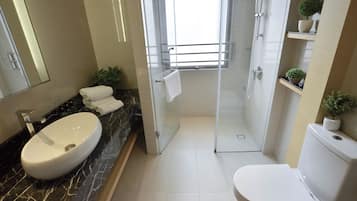 A modern bathroom with a marble sink, a toilet, and a glass-enclosed shower.