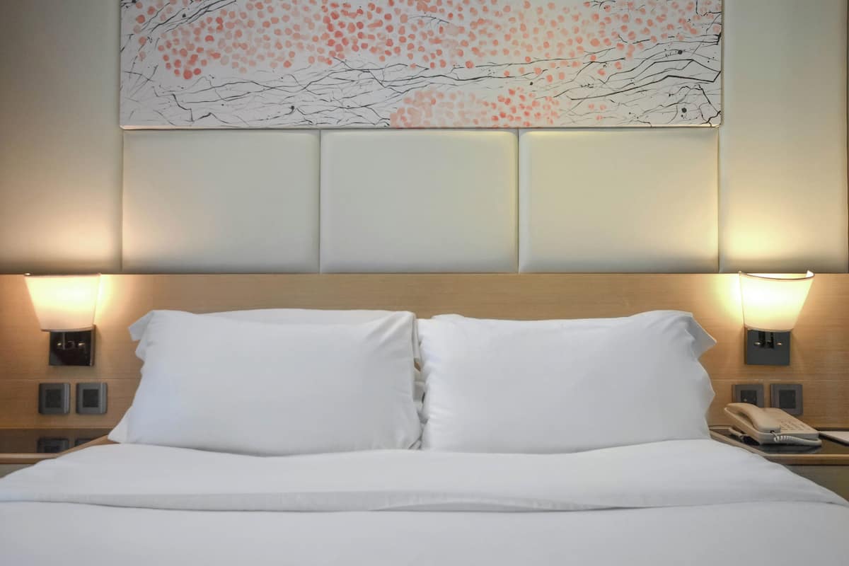 A hotel room with a large bed, two bedside lamps, a phone, and a wall-mounted artwork.