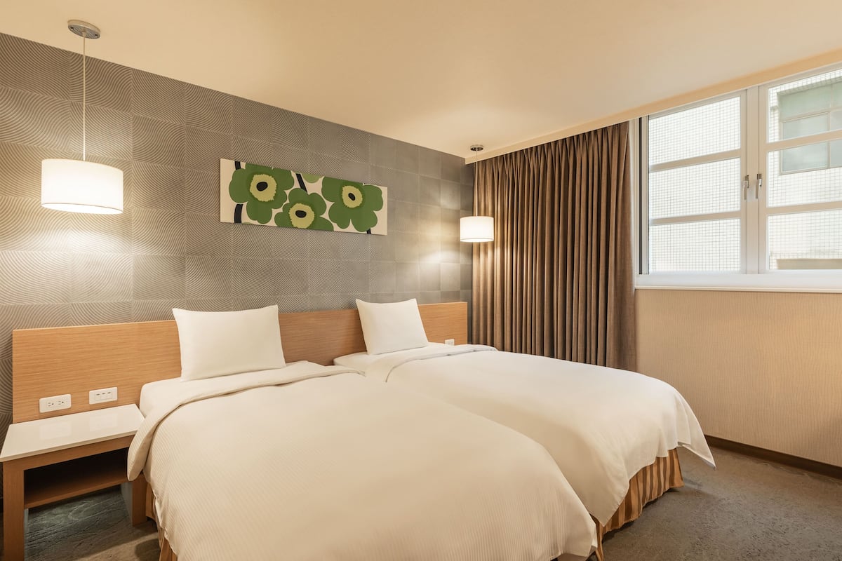 Une chambre d’hôtel avec un lit double, deux tables de chevet, une œuvre d’art accrochée au mur, une fenêtre avec des rideaux et un mur à motifs.