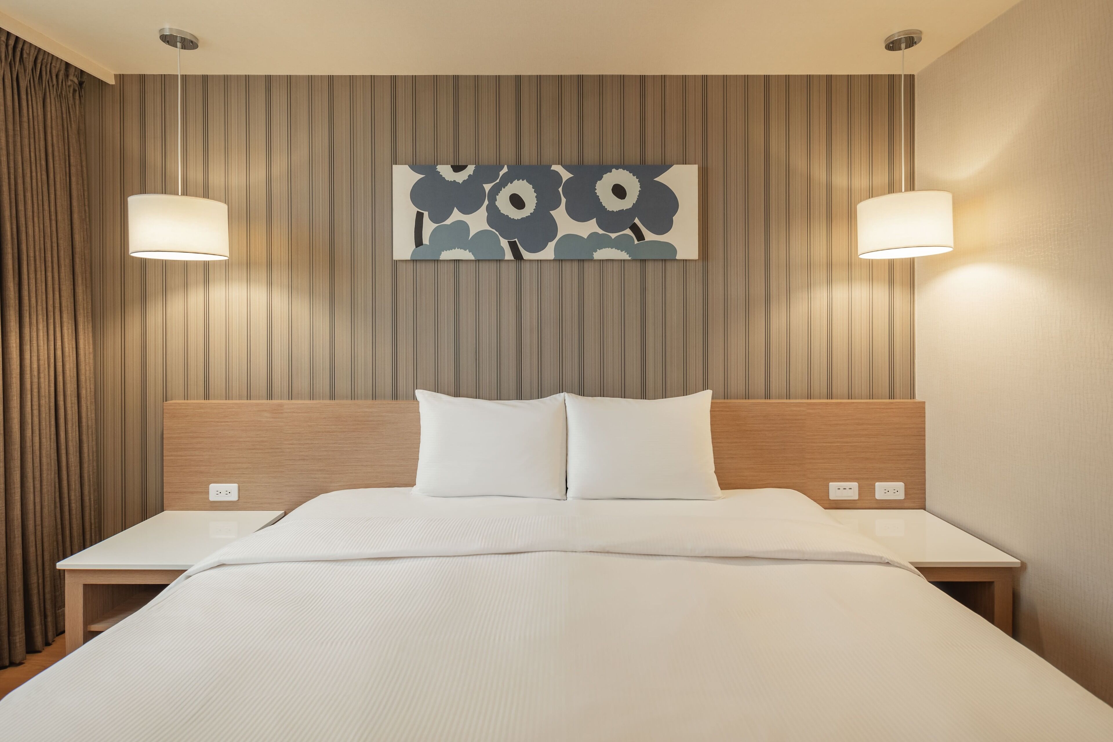 A hotel room with a large bed, two bedside tables, a headboard, and a wall-mounted artwork.