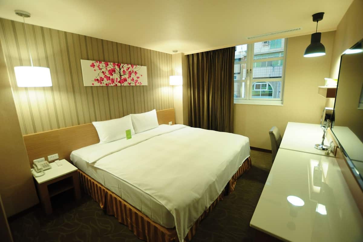 Une chambre d’hôtel avec un lit, une table de chevet, une lampe et une fenêtre avec des rideaux.