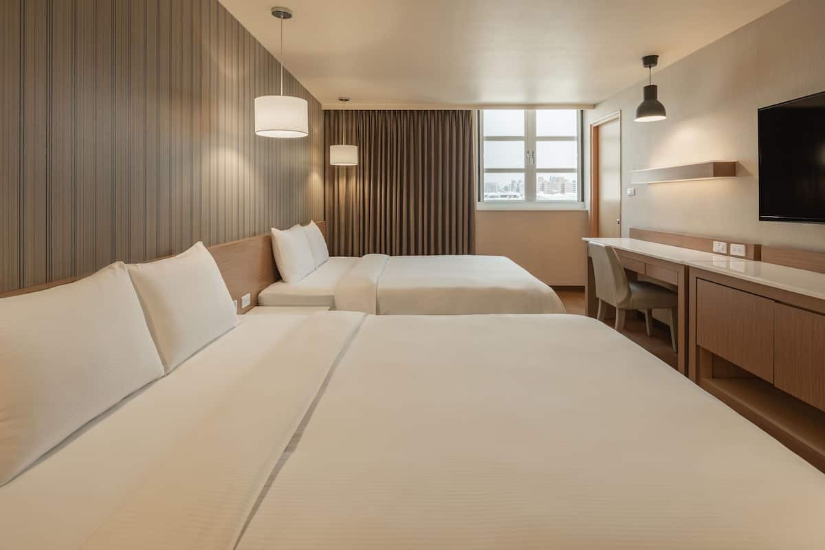 Une chambre d’hôtel avec deux lits, un bureau, une chaise, une télévision et une fenêtre donnant sur la ville.