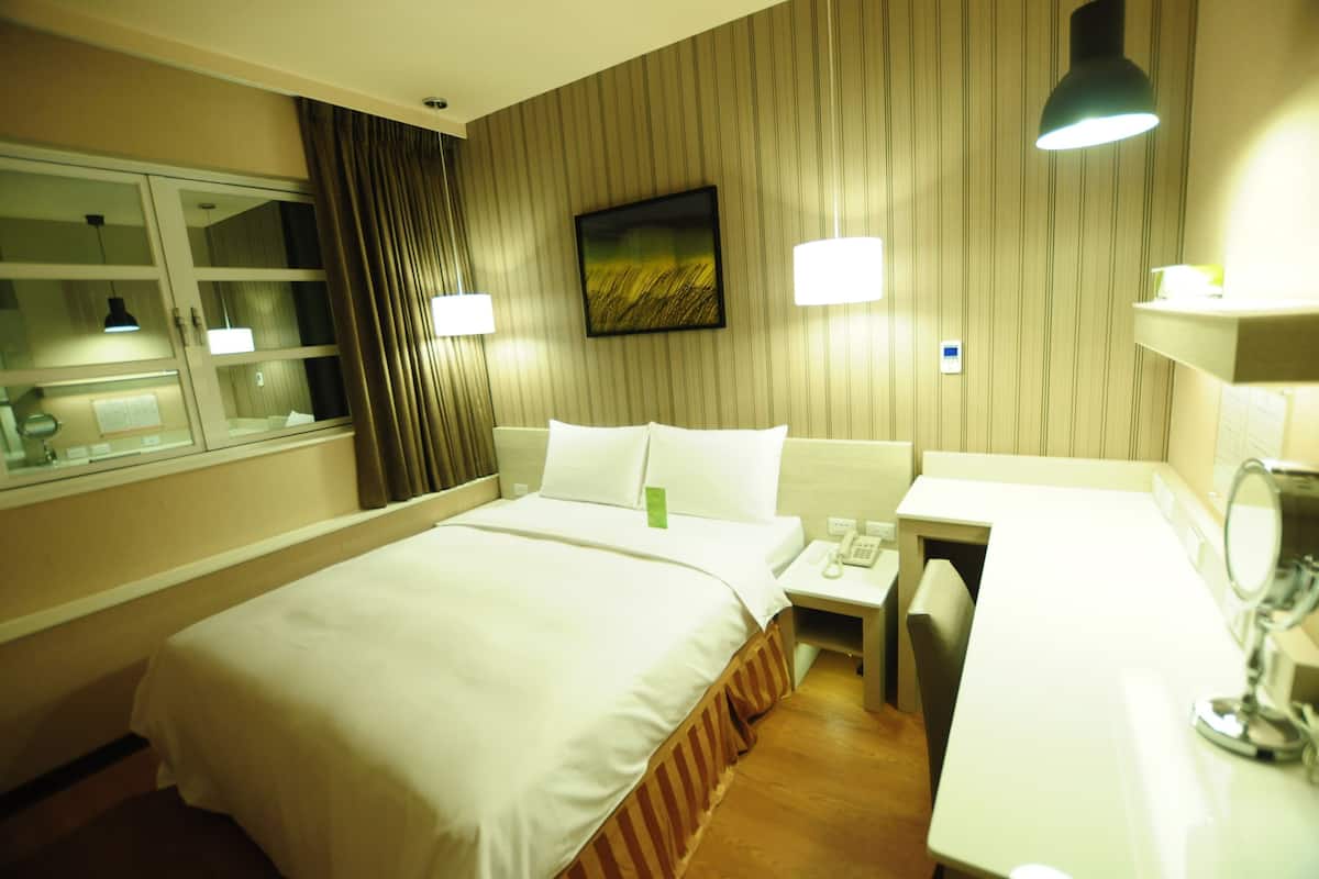 Une chambre d’hôtel avec un lit, une table de chevet, une lampe et un miroir.