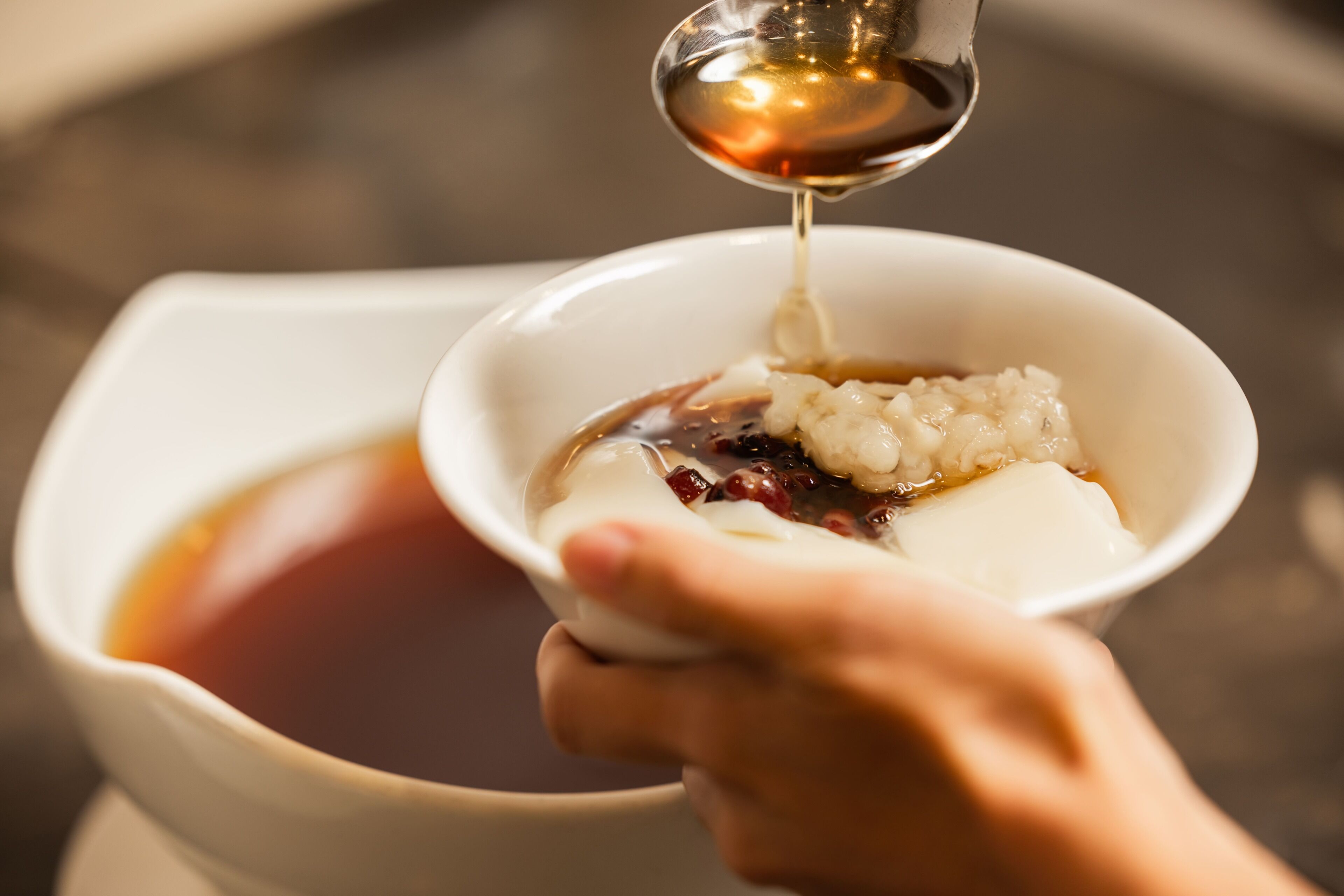 A hand holding a bowl with a beverage being poured into it.