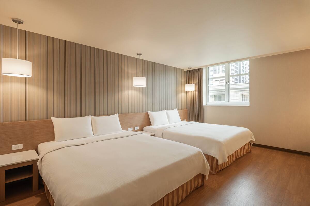 Une chambre d’hôtel avec deux lits, une tête de lit en bois, une fenêtre avec des rideaux et un mur orné de motifs verticaux.