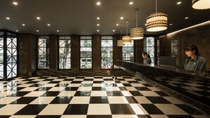 Un hall d’hôtel avec un sol à carreaux, de grandes fenêtres et un éclairage moderne suspendu au plafond.