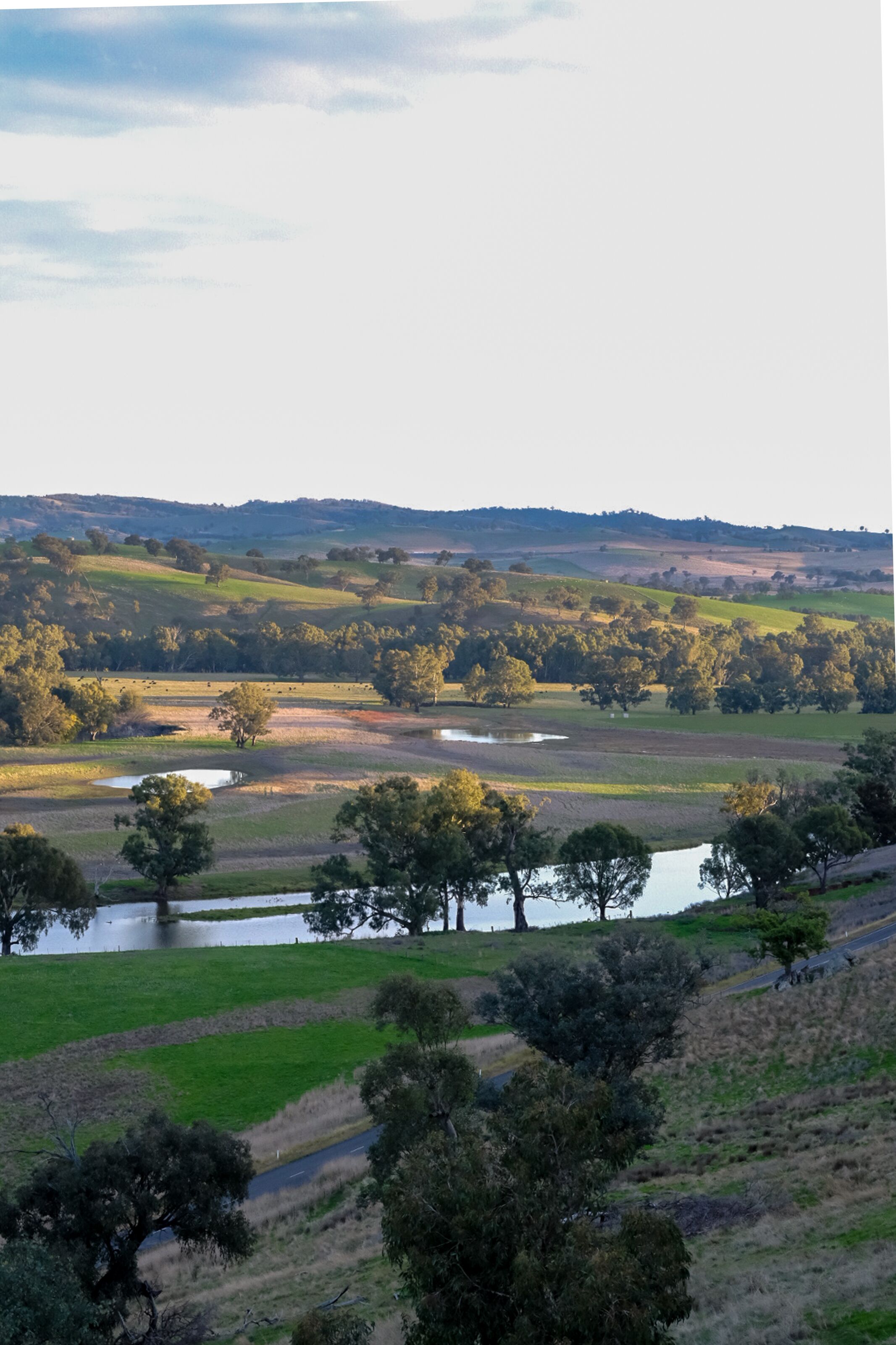A panoramic view of a countryside landscape with rolling hills, a river, and scattered trees.