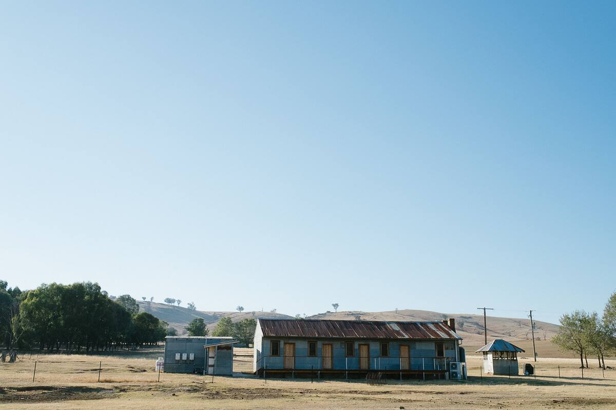 A small, single-story building with a blue exterior and a metal roof, surrounded by a fenced area and sparse vegetation.