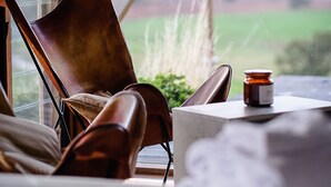 A room with a view of a green landscape, a wooden-framed window, a brown leather chair, a small table with a candle, and a white decorative item. - Kimo Estate (Nangus)