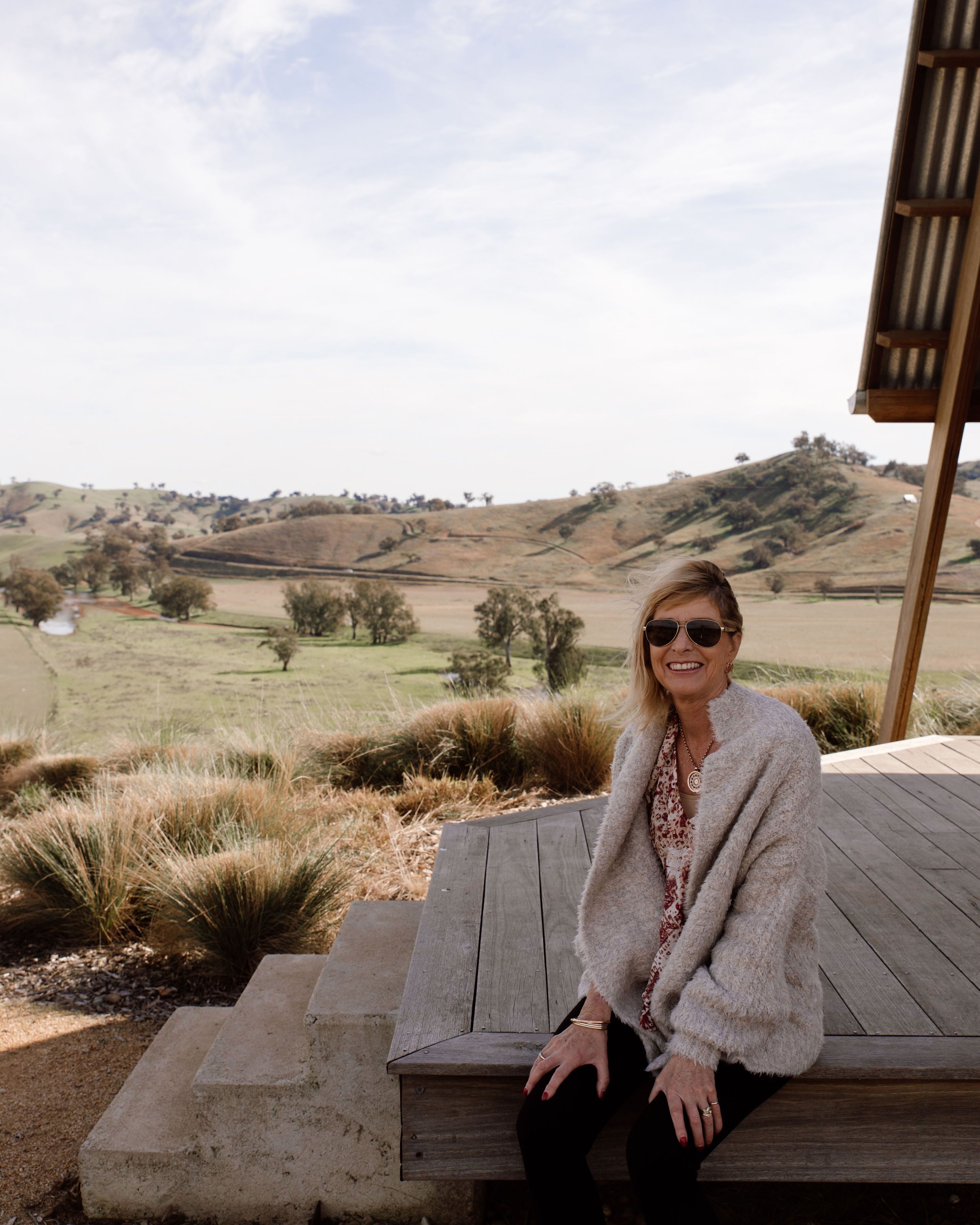 A person sitting on a wooden deck with a view of rolling hills and sparse trees in the background.