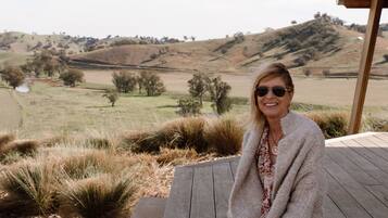 A person sitting on a wooden deck with a view of rolling hills and sparse trees in the background.
