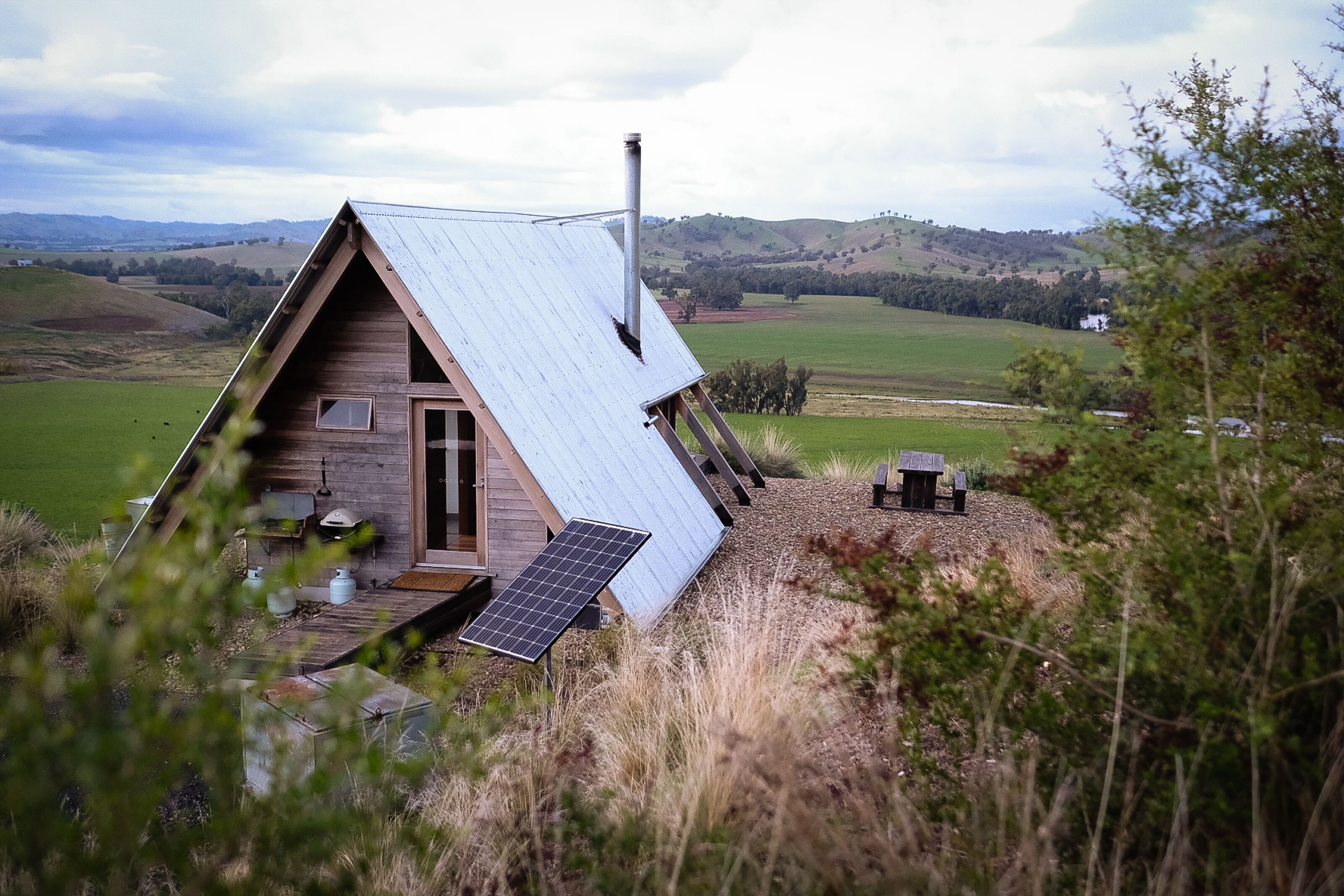 Eine Holzhütte mit geneigtem Dach, Schornstein und einer Solaranlage.