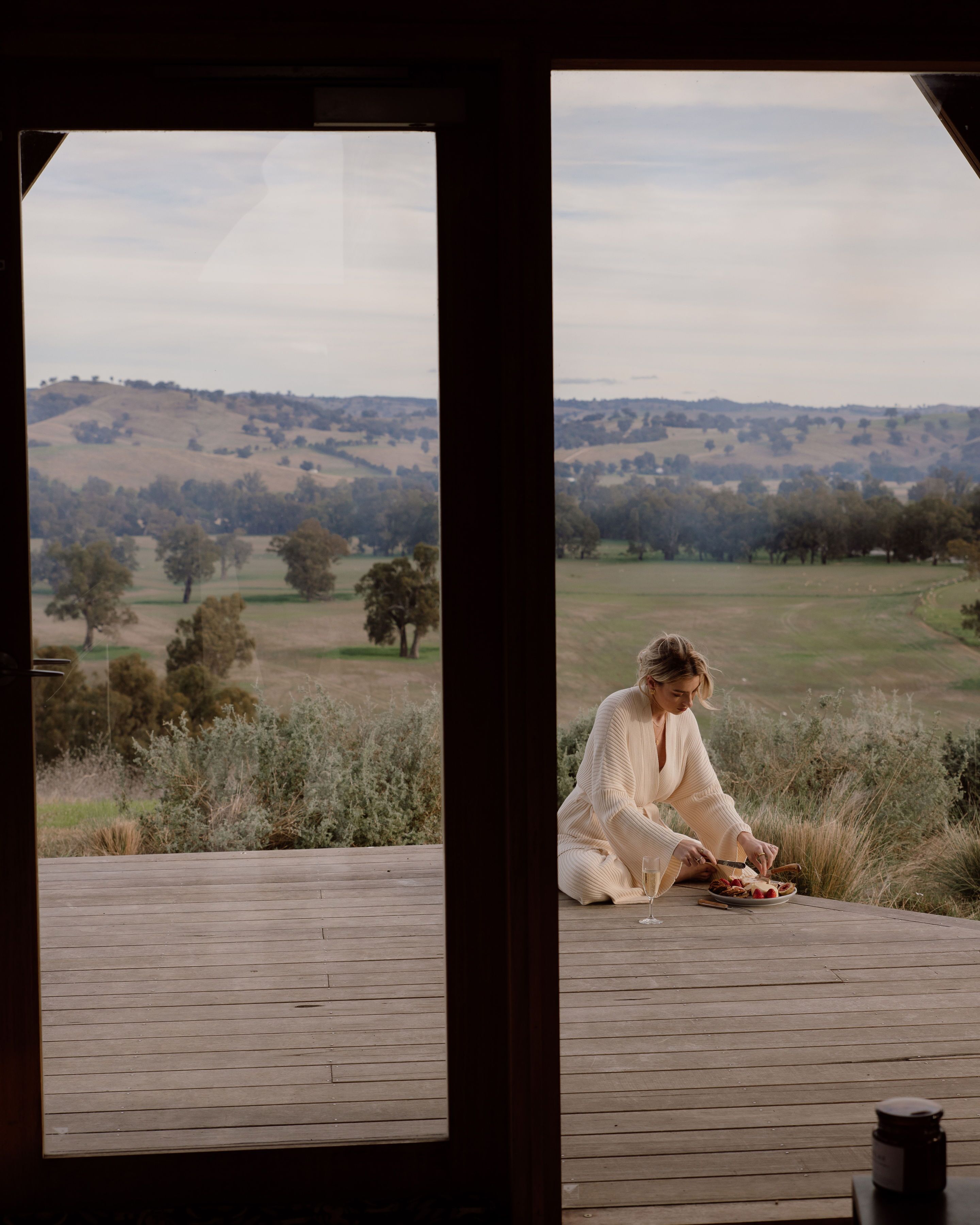 A person sitting on a wooden deck with a scenic view of rolling hills and trees.