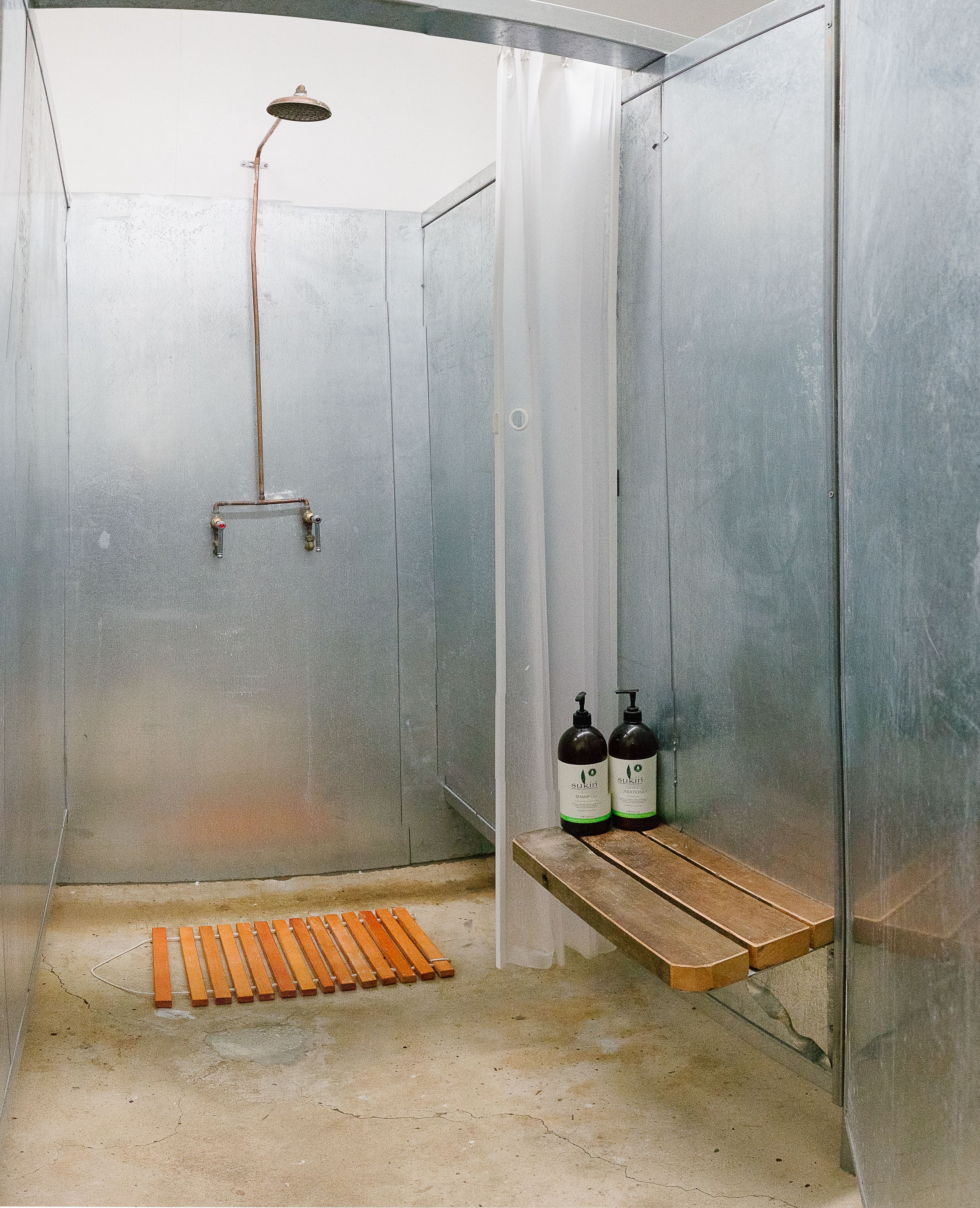 Ducha con cabezal de ducha manual, un banco de madera y dos botellas de champú en un estante.