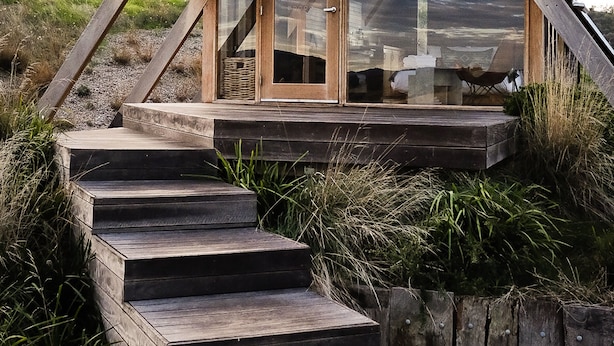 A modern, triangular-roofed building with a wooden staircase leading to a glass door entrance. - Kimo Estate (Nangus)