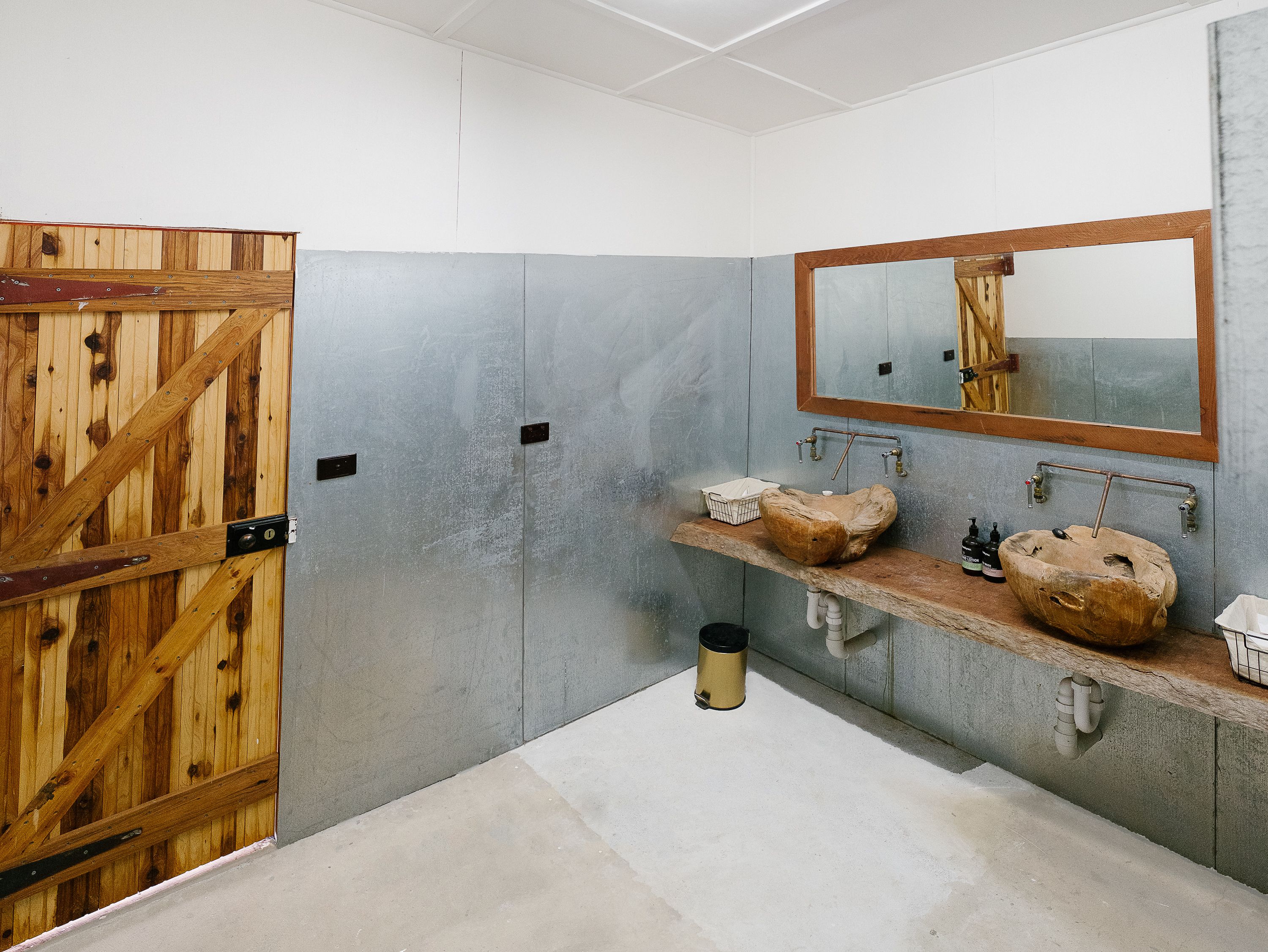 Une salle de bain avec une porte en bois, un grand miroir et un lavabo en pierre.