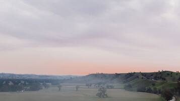 Ländliche Landschaft mit sanften Hügeln, einem weiten Feld und einer kleinen Holzhütte im Vordergrund.