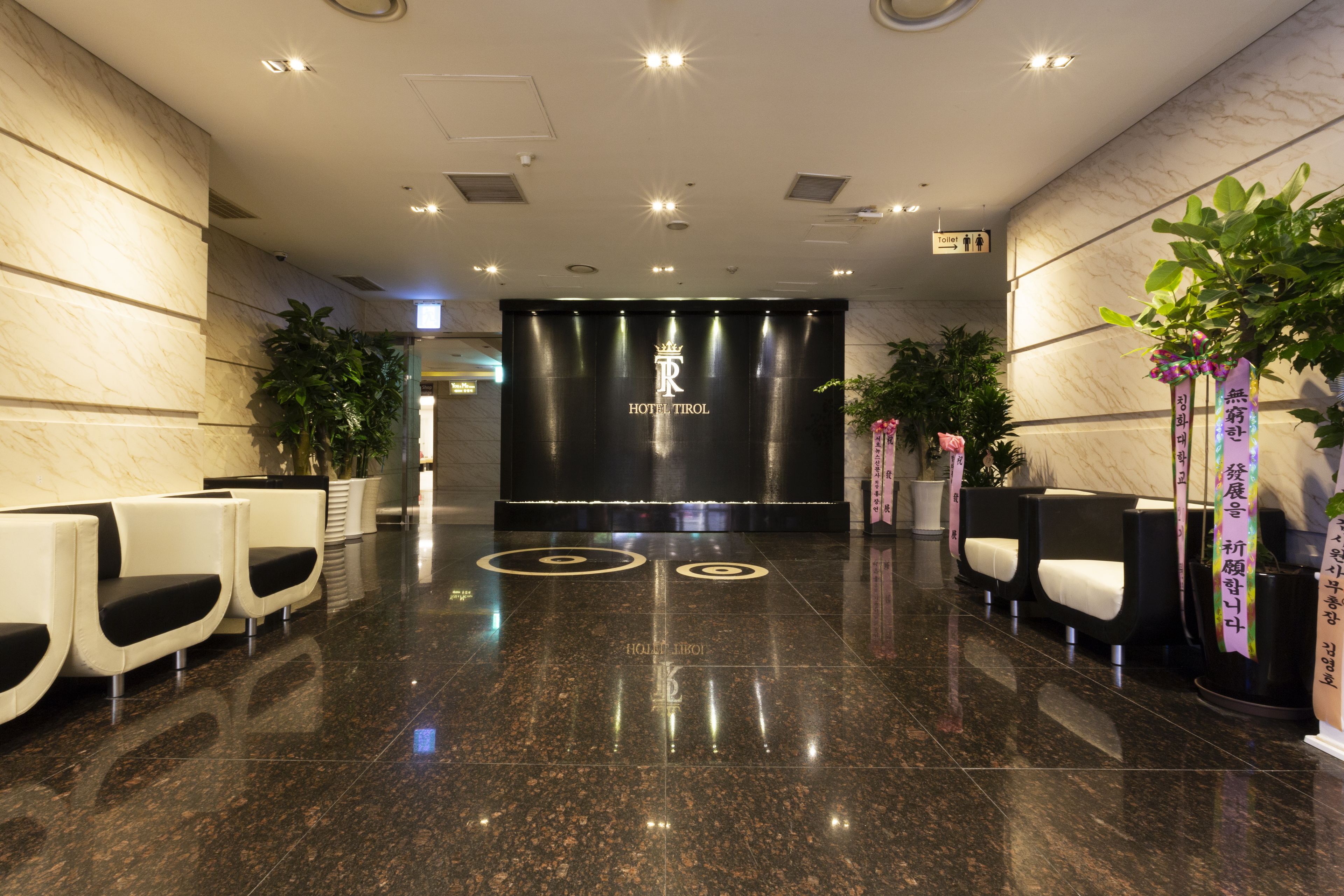 A hotel lobby with a reception desk, seating area, and a sign indicating the location of the toilet.