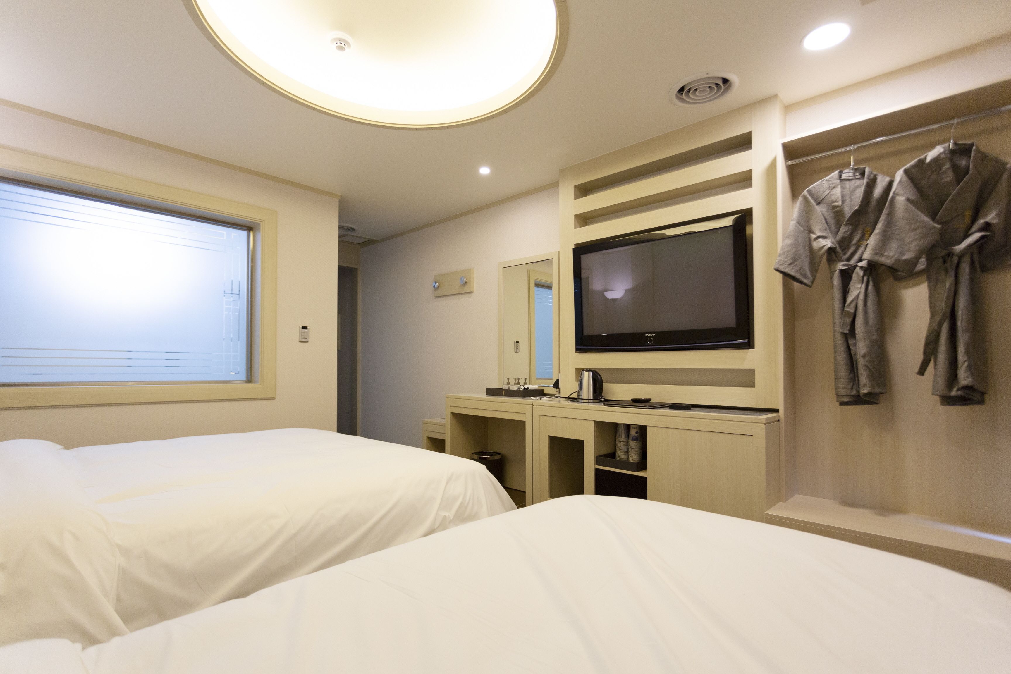 A hotel room with two beds, a television, a minibar, and a robe rack.