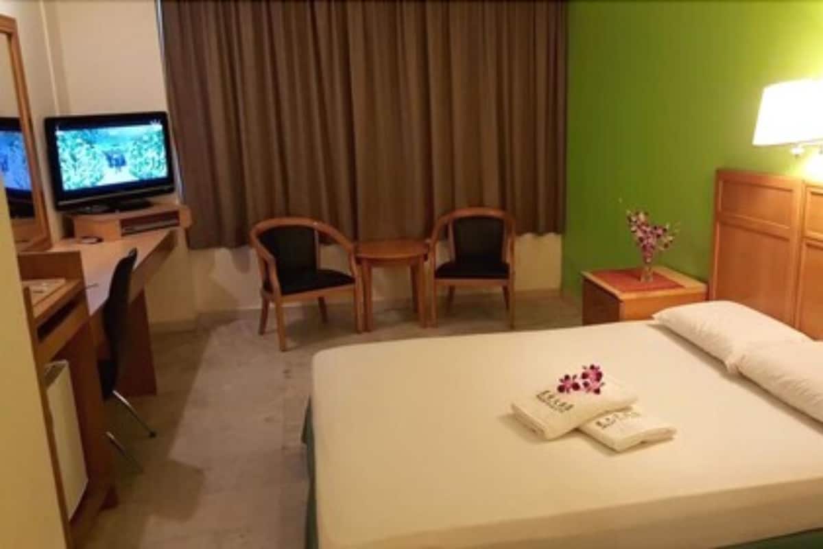 A hotel room with a bed, two chairs, a desk with a computer, a nightstand with a lamp, and a green wall.