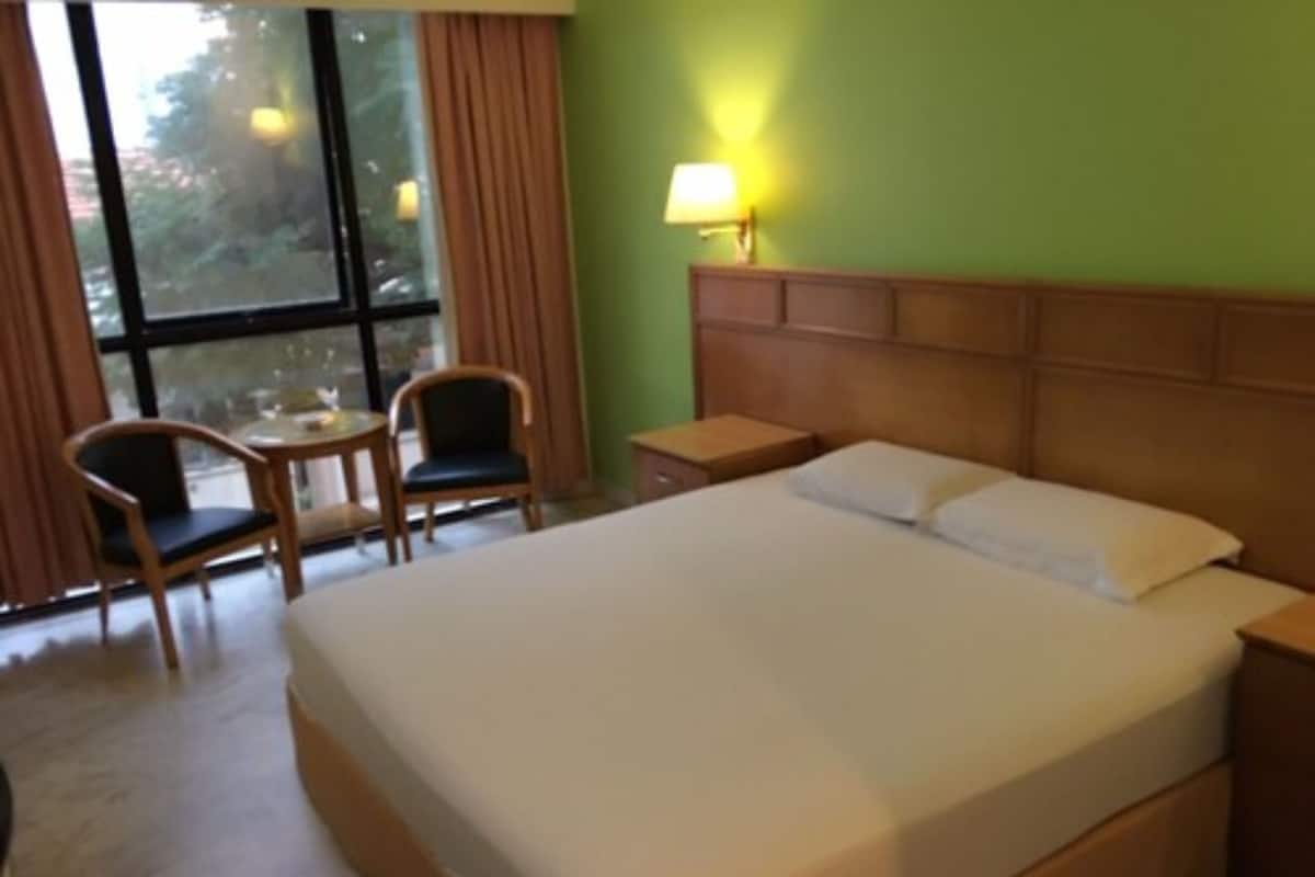 A hotel room with a large bed, a small table, two chairs, a nightstand, and a window with curtains.